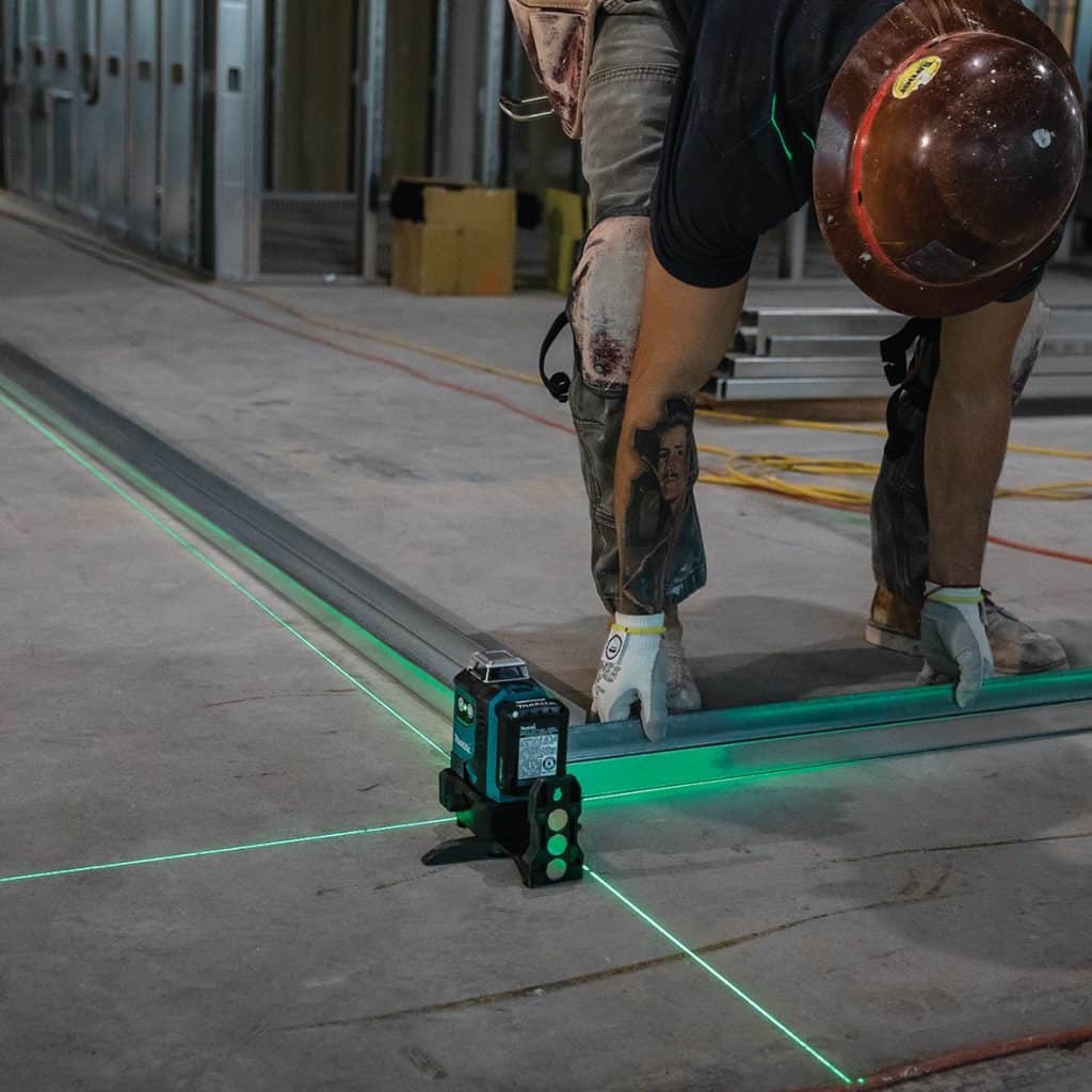 Makita SK700GD / SK700GDWA – Professional Green Laser Level on a job site projecting green laser while a tradeperson sets out flooring track