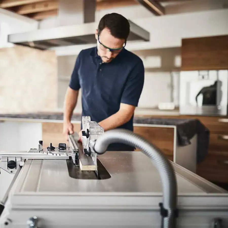 “Person running a piece of melamine through a table saw while wearing safety glasses, working in a kitchen installation environment.”