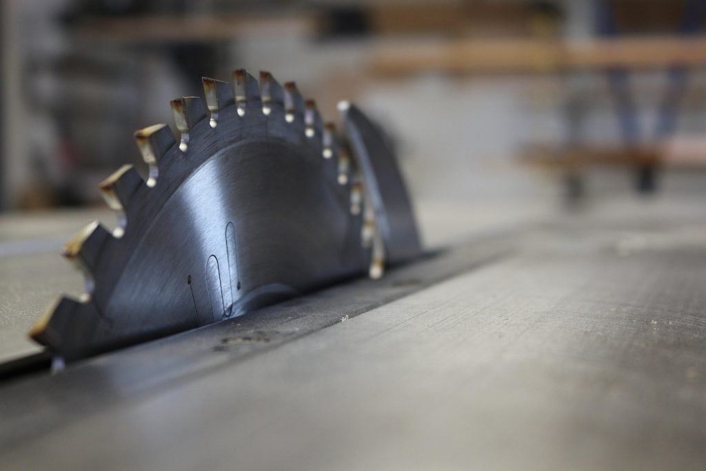 Close-up of a table saw blade with a riving knife visible, showing the exposed teeth without a guard attached.”