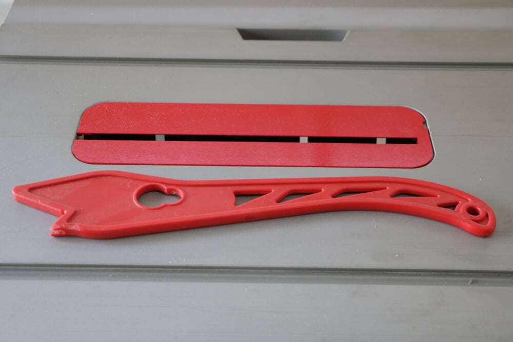 Table saw surface with a red push stick resting beside the blade opening