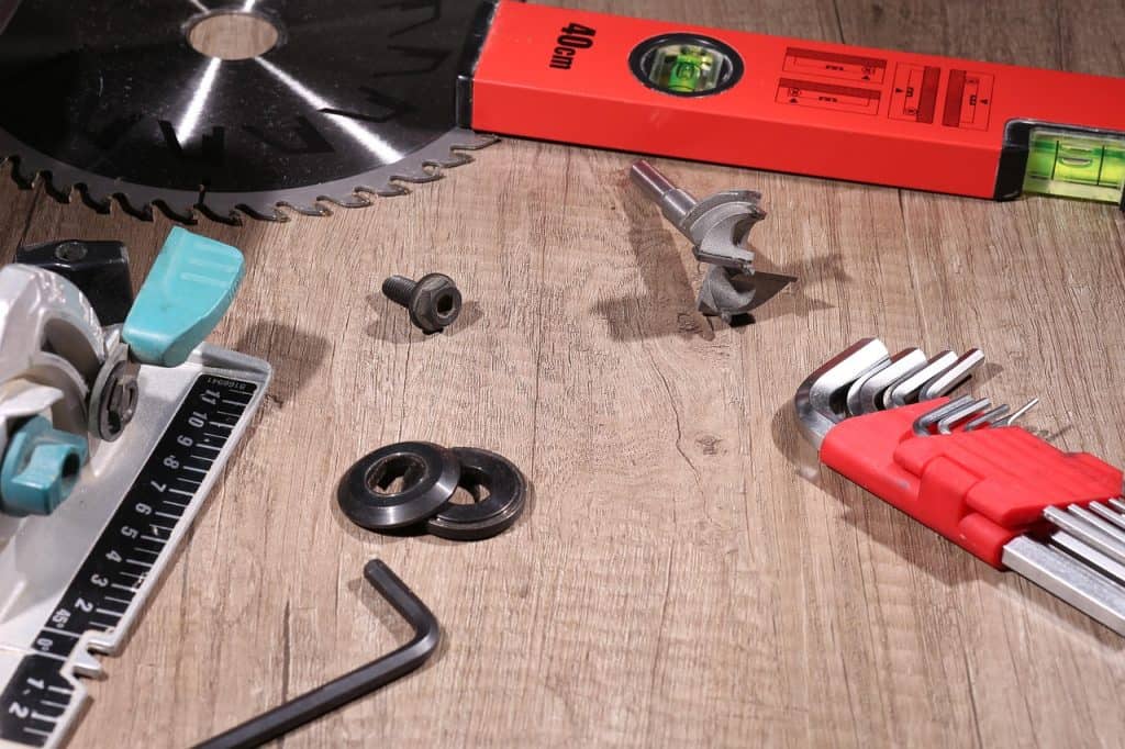 Assorted woodworking tools including a saw blade, Allen keys, drill bit, level, and handheld circular saw laid out on a surface
